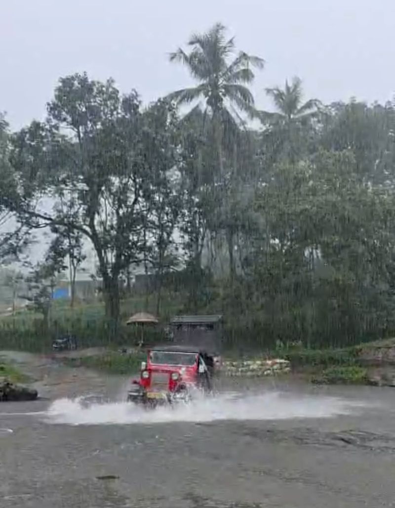 A red jeep driving through a shallow river crossing in heavy rain