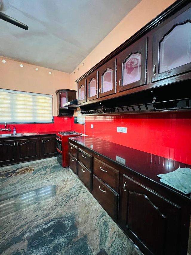 The kitchen: dark wooden cabinets above and below a long black counter, a red splashback, a gas cooker and a sink under the window