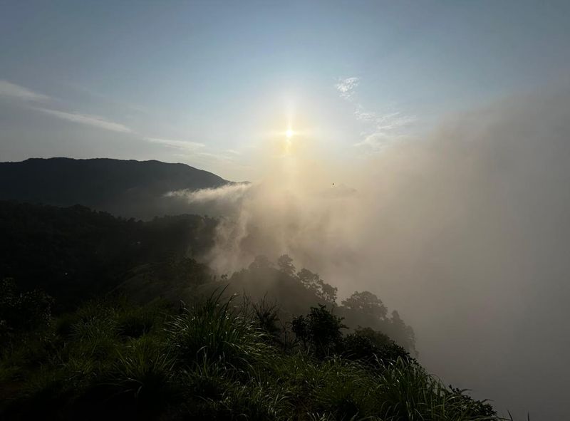 The sun above a bank of cloud pouring over a dark hillside